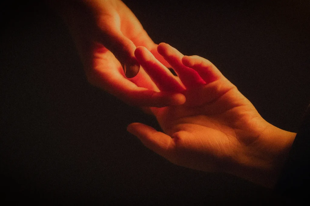 Close-up of two hands gently reaching toward each other in warm light, symbolizing compassion, emotional support, human connection, hope, and care.
