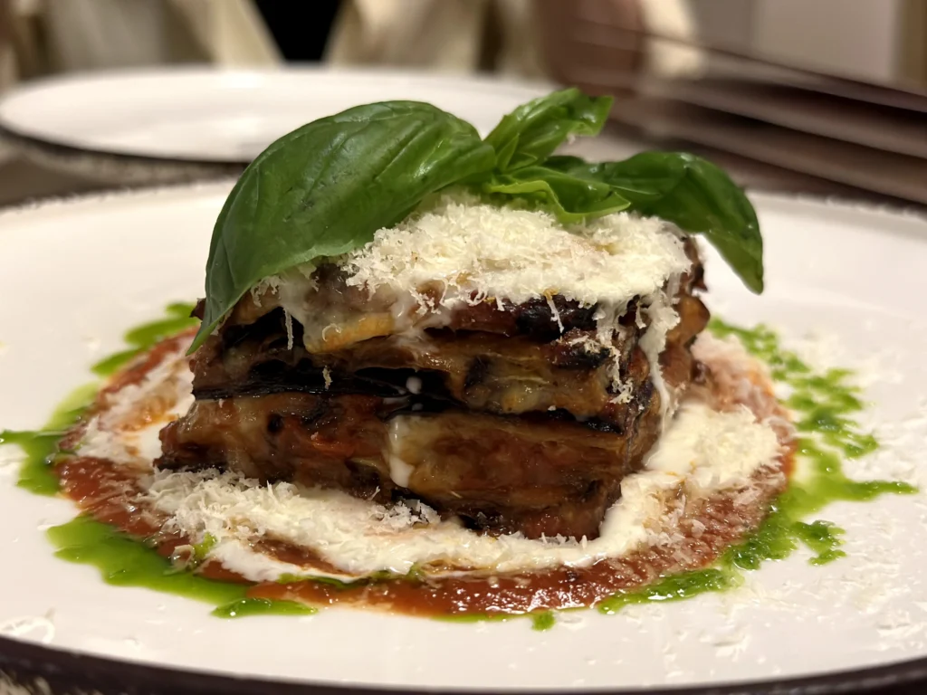 Layered eggplant parmigiana served with rich tomato sauce, creamy cheese, fresh basil, and grated Parmesan at Bacio Italian Restaurant.