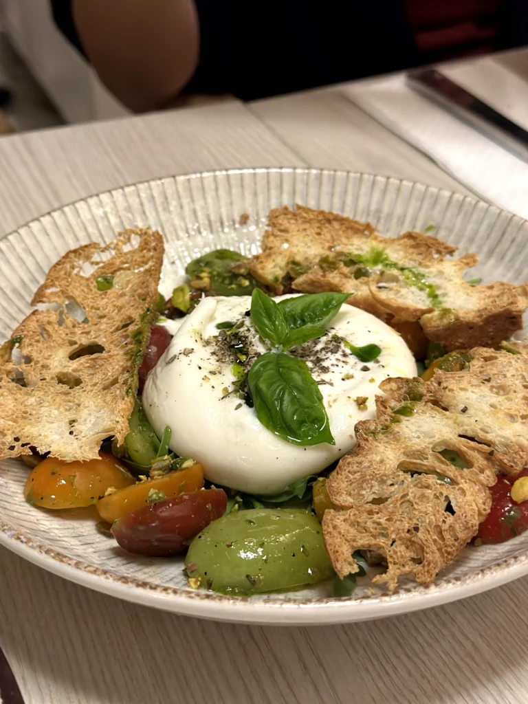 Fresh burrata salad topped with basil, heirloom tomatoes, toasted artisan bread, olive oil, and cracked black pepper at Bacio Italian Restaurant.