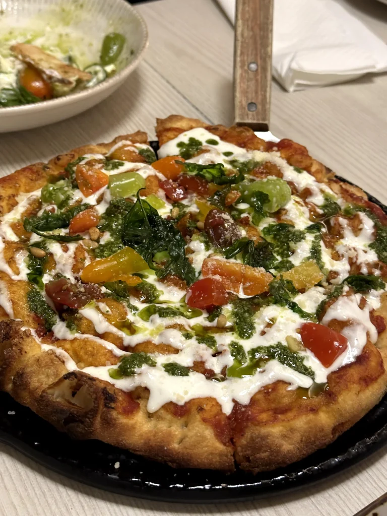 Wood-fired burrata and basil pesto pizza topped with heirloom cherry tomatoes, fresh basil, pine nuts, and creamy burrata at Bacio Italian Restaurant.