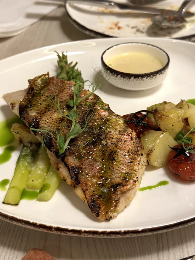 Pan-seared fish fillet served with roasted potatoes, asparagus, blistered cherry tomatoes, herb oil, and a creamy sauce at Bacio Italian Restaurant.