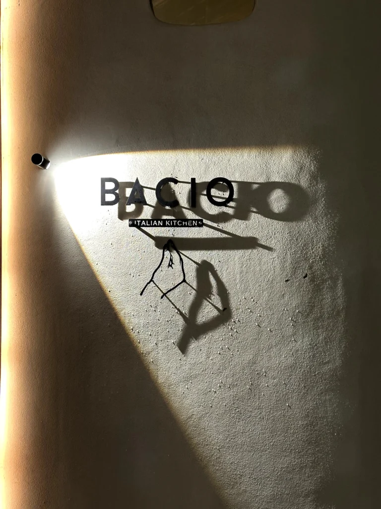 Bacio Italian Kitchen illuminated wall logo with minimalist signage and warm ambient lighting at the restaurant entrance.